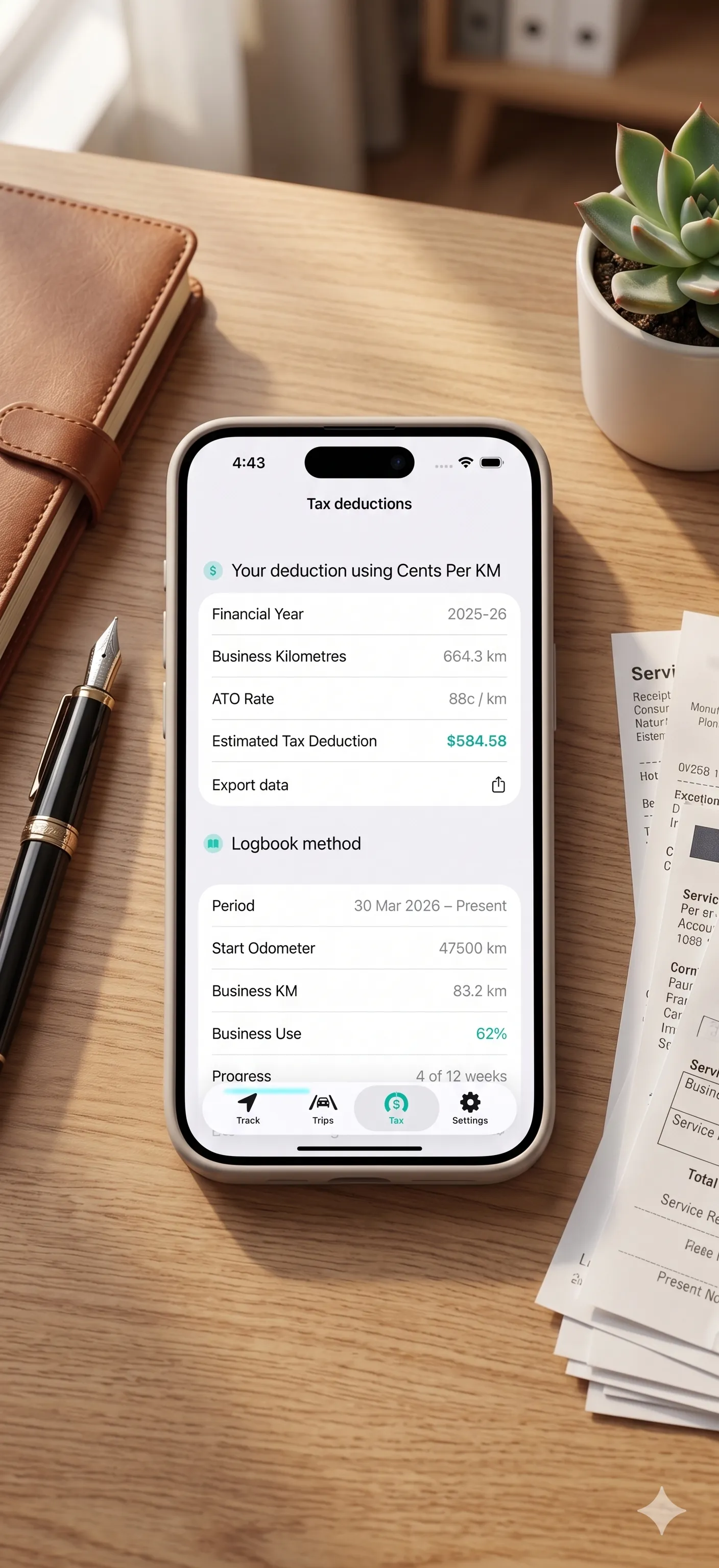 An iPhone showing the Trax tax deductions screen, sitting on a wooden desk next to receipts and a fountain pen